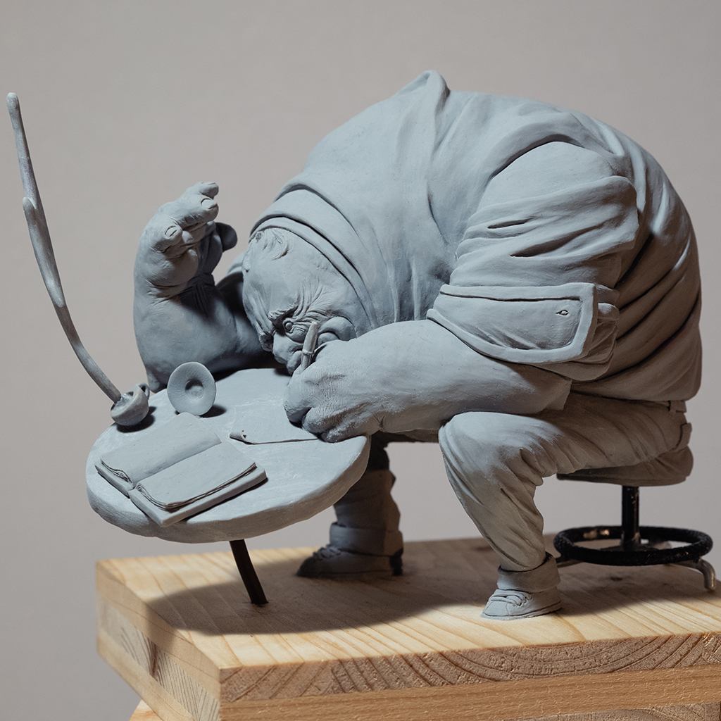 Sculpture de l'artiste Teddy Ros "café-créa" 2022, sculpté en pâte polymère , représentant un gros personnage assis sur un tabouret en train d'écrire dans son petit carnet, alors que sa tasse de café vol en éclat image 1