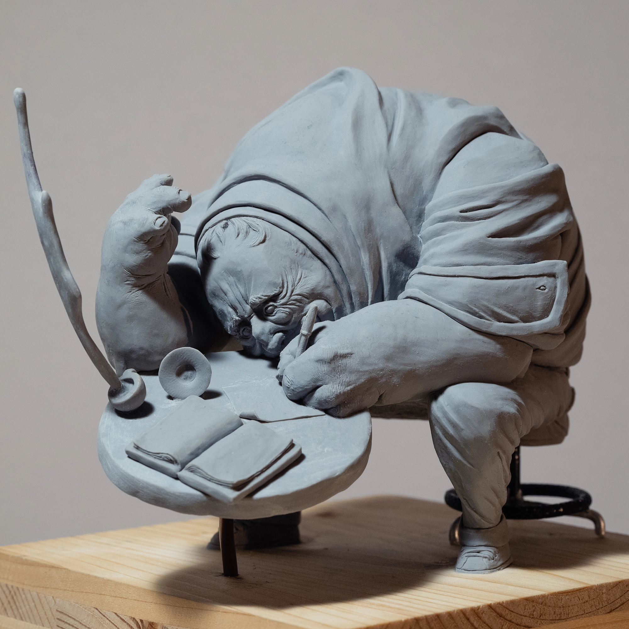 Sculpture by the artist Teddy Ros "café-créa" 2022, sculpted in polymer clay, representing a large character sitting on a stool writing in his little notebook, while his cup of coffee is shattered, Teddy Ros artist contemporary art series